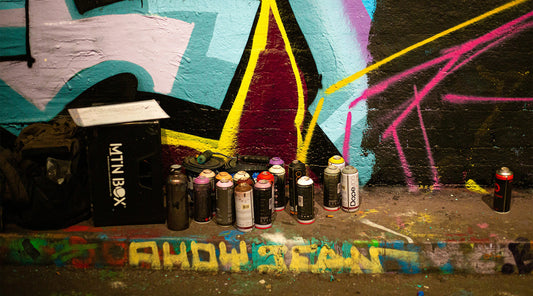 Assortment of vibrant spray paint cans in front of a colorful graffiti wall, showcasing top brands for canvas, mural, and clothing art.