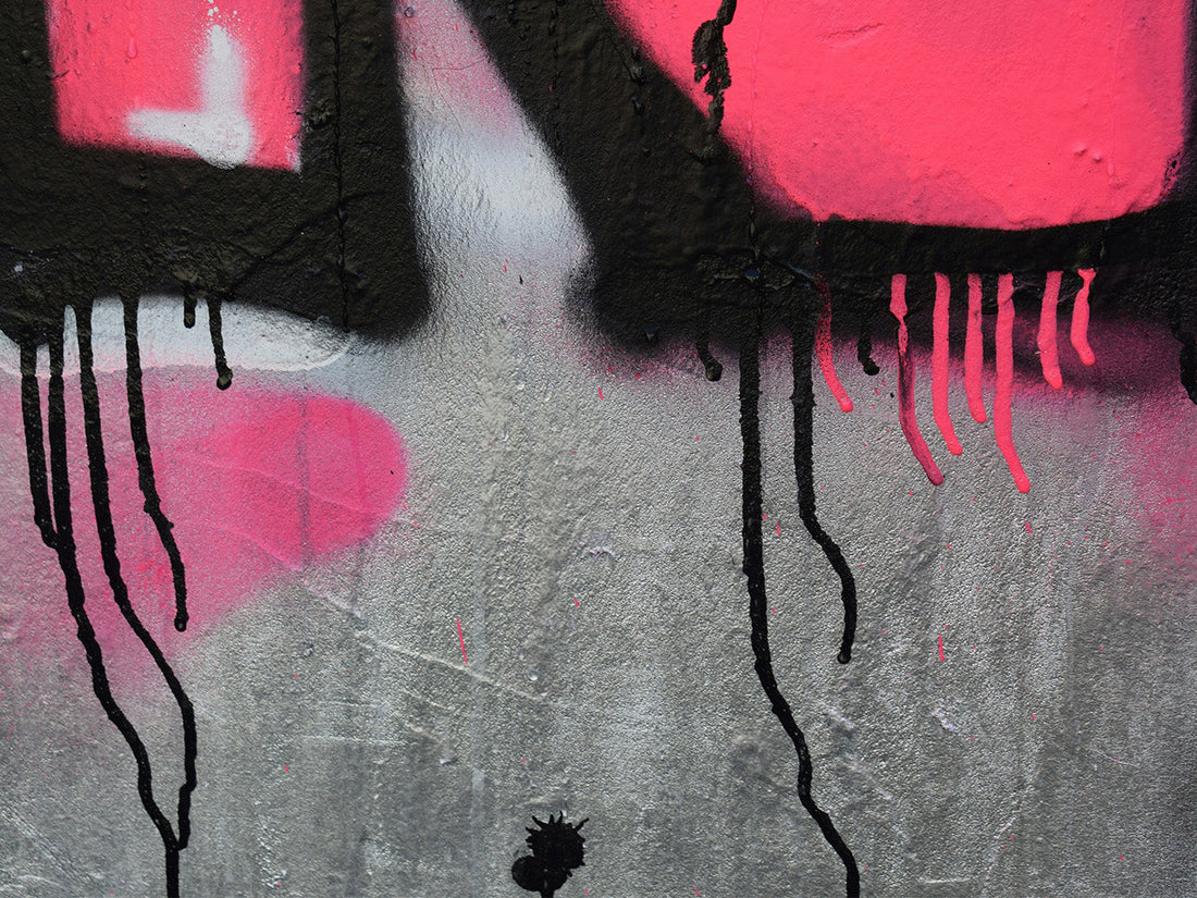Graffiti detail showing dripping spray paint lines in black over pink background on rough wall